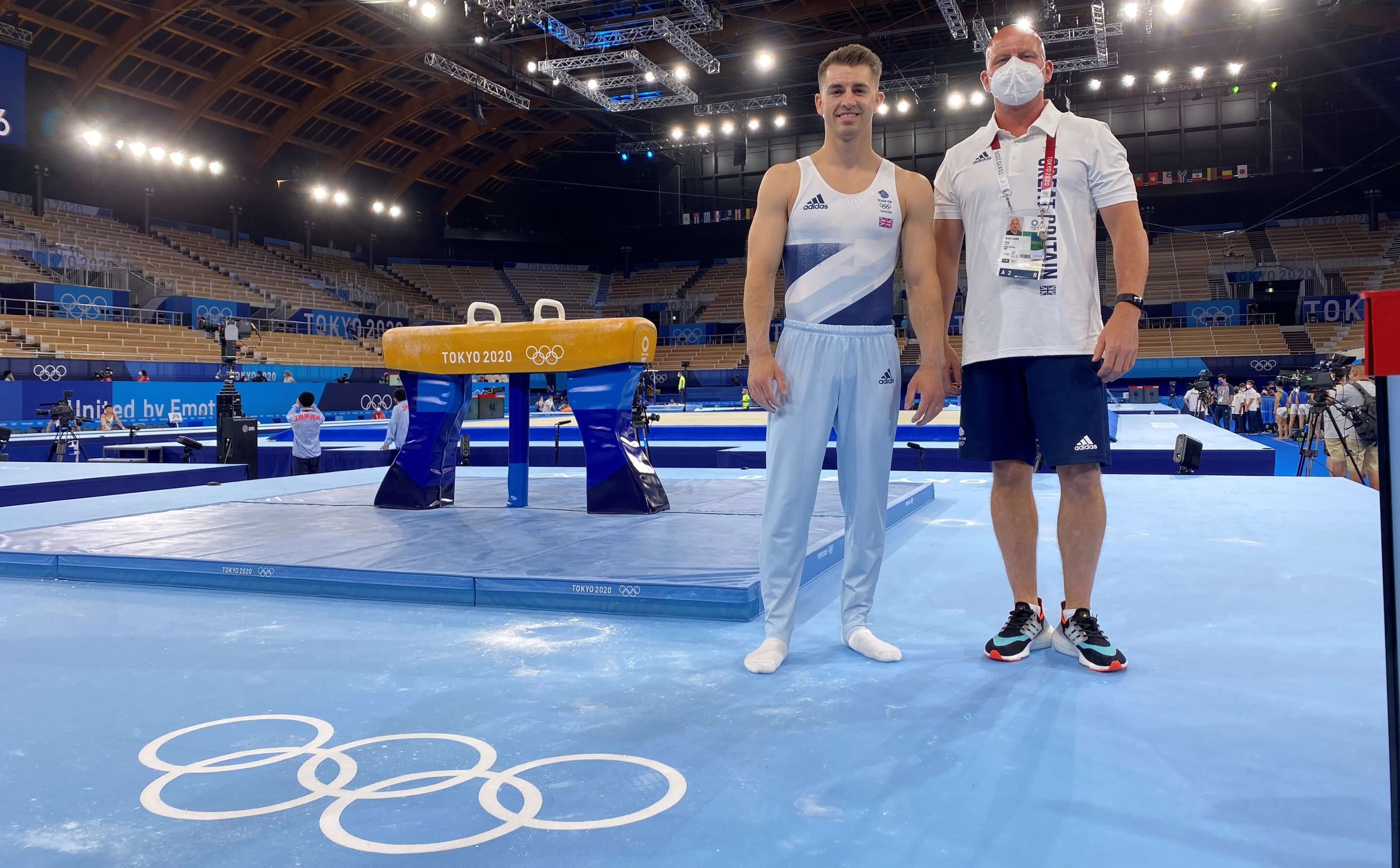 Coach and gymnast pose for a photo in front of the pommel horse apparatus inside the Olympic Games gymnastics venue