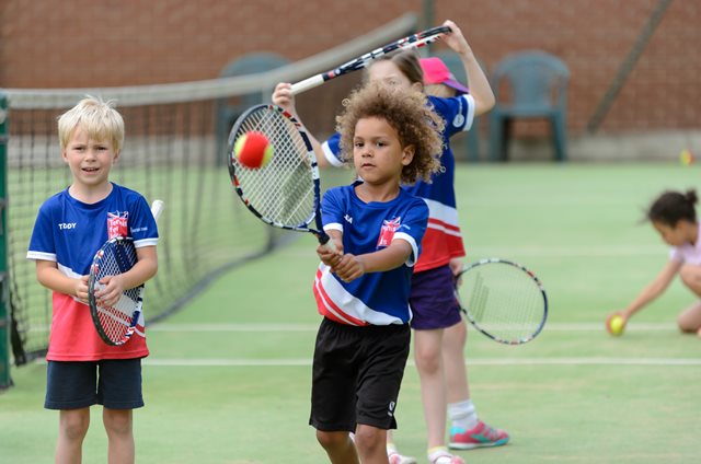 A young tennis player smashes a forehand during a group activity