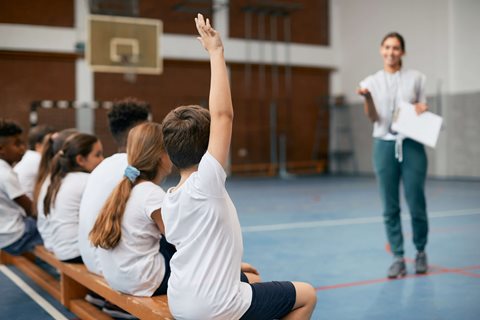 Boy sat on a bench in a sports hall putting his hand up to ask a question