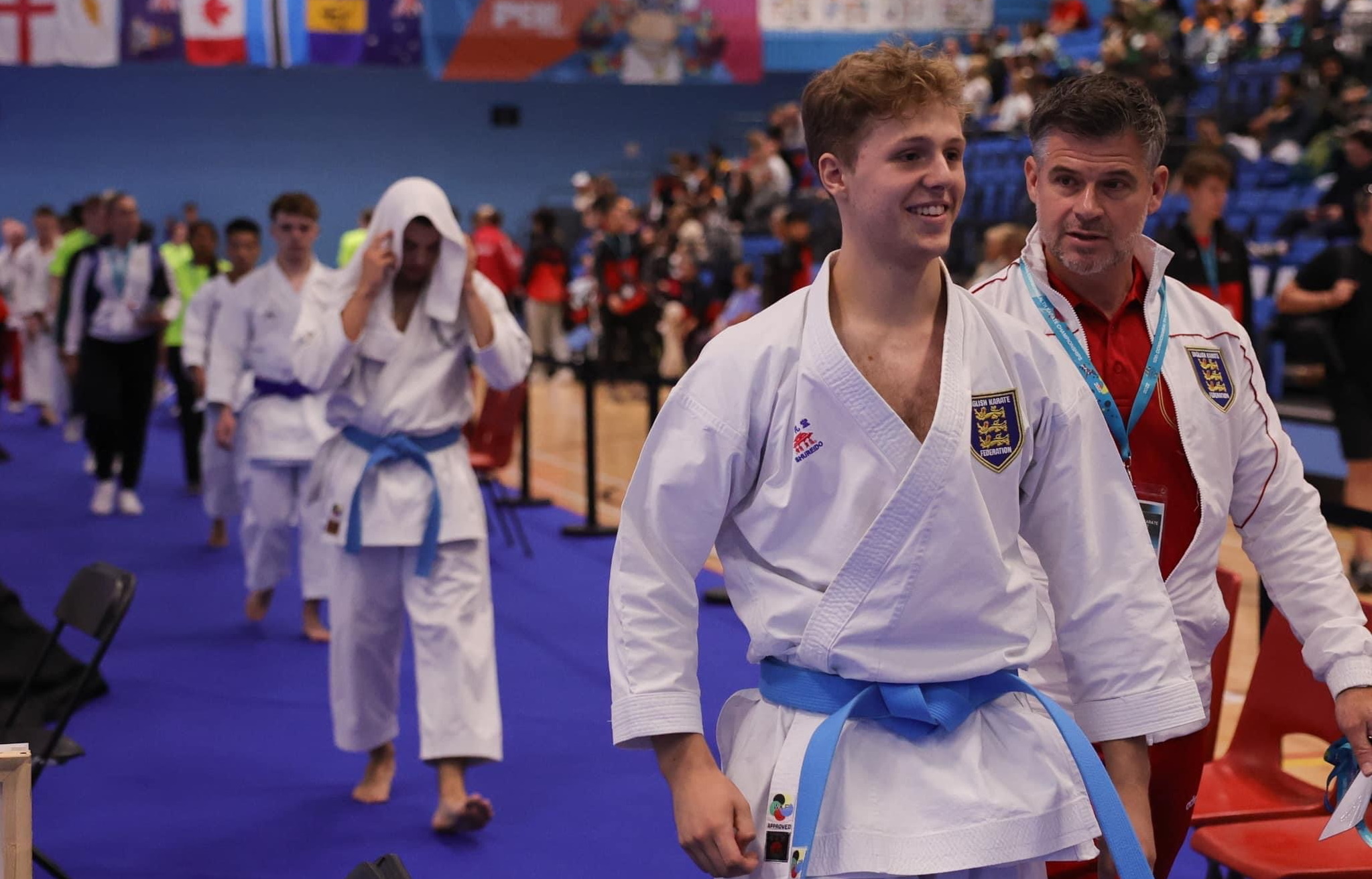 Coach walking into the sports hall during a competition talking to a karate student wearing a blue belt