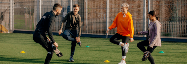 A happy group of people doing a touch heel exercise, each one bringing their feet up in their own unique way