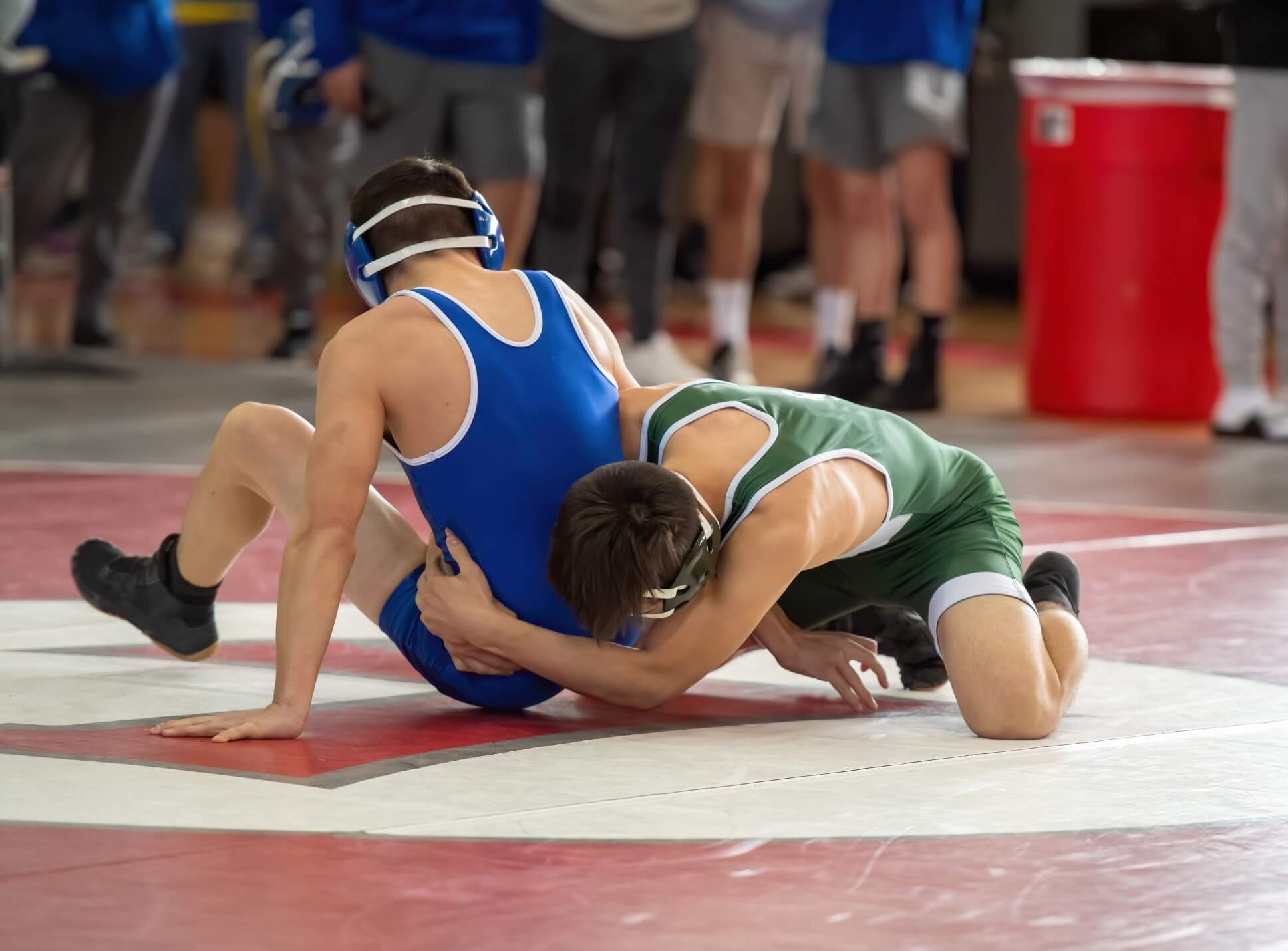 Two teenage boys are on a red wrestling mat wrestling in on the ground